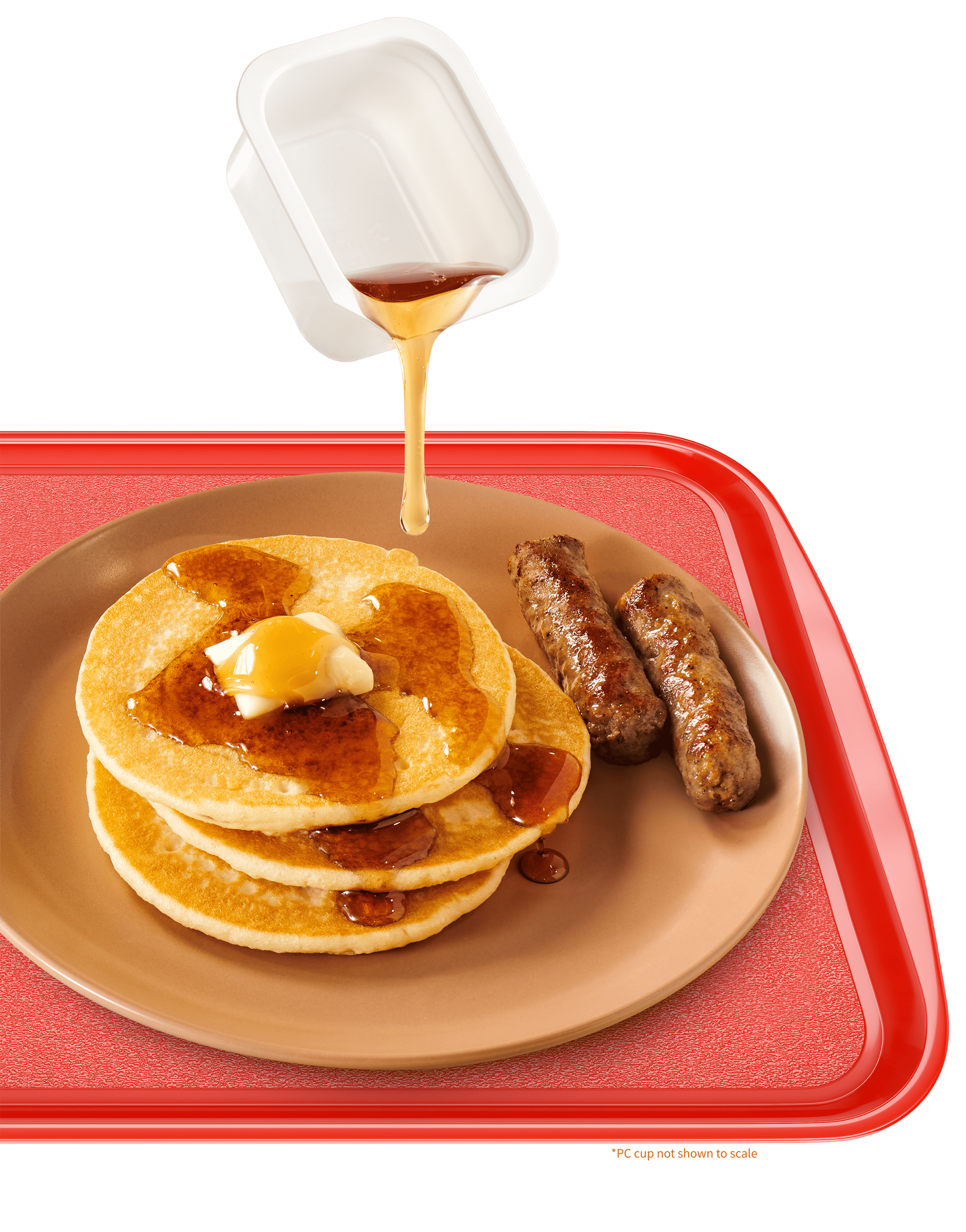 A plate with three pancakes topped with butter and syrup, two sausages on the side, and syrup being poured from a small cup, all on a red tray. PC Cup not shown to scale.