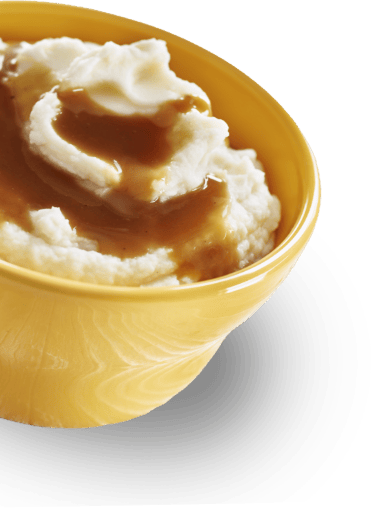 A yellow bowl filled with creamy mashed potatoes topped with brown gravy.